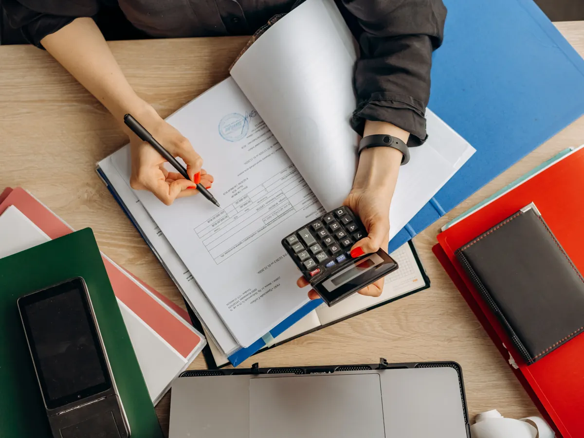 Persona revisando documentos con una calculadora sobre el escritorio.