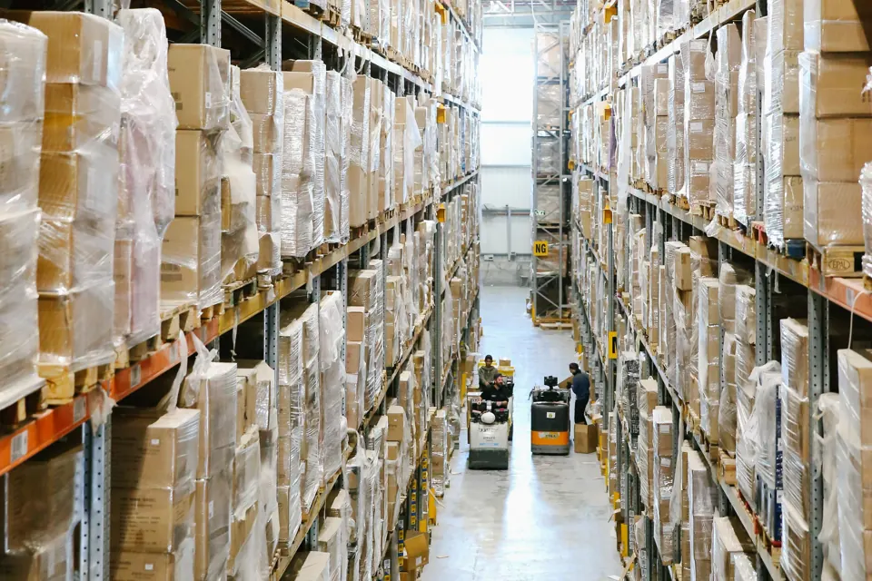Estanterías con cajas y trabajadores en el pasillo de un depósito.